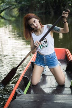An adventurous young woman paddles a boat in a serene river surrounded by lush greenery.