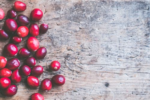 Free Bright red cranberries scattered on a rustic wooden surface, offering a natural and textured background. Stock Photo