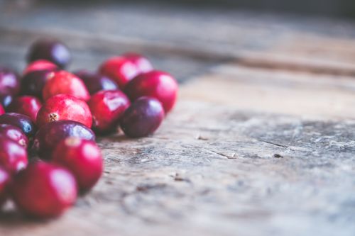 Free A rustic close-up view showing vibrant red cranberries scattered on a wooden surface. Stock Photo