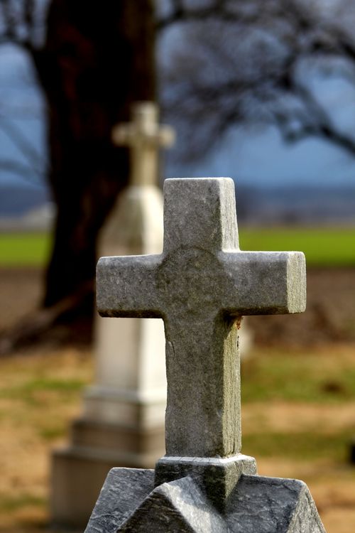 Free Weathered cross tombstone in outdoor rural cemetery with blurred background for serene remembrance. Stock Photo