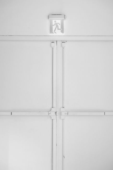Clean minimalist design featuring white double doors with an emergency exit sign overhead.