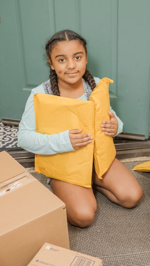 Free Smiling girl with braided hair holding delivery packages at home doorstep. Stock Photo