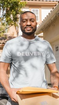 A smiling delivery man holding parcels in a sunny outdoor setting, representing reliable service.