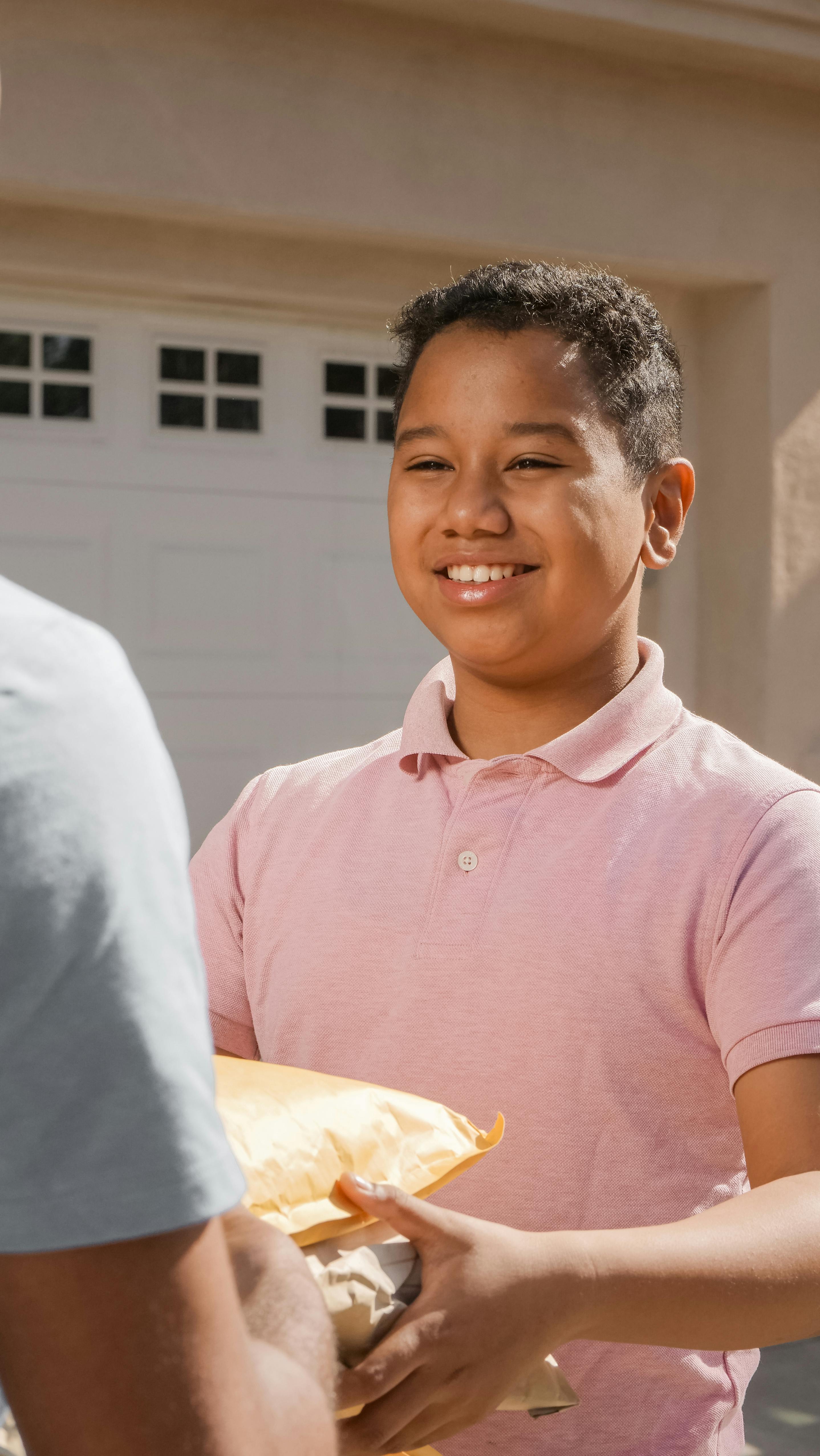 man in pink shirt holding brown package smiling