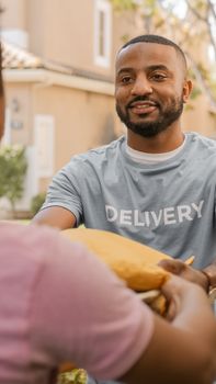 Smiling deliveryman in uniform handing a package to a customer outdoors.