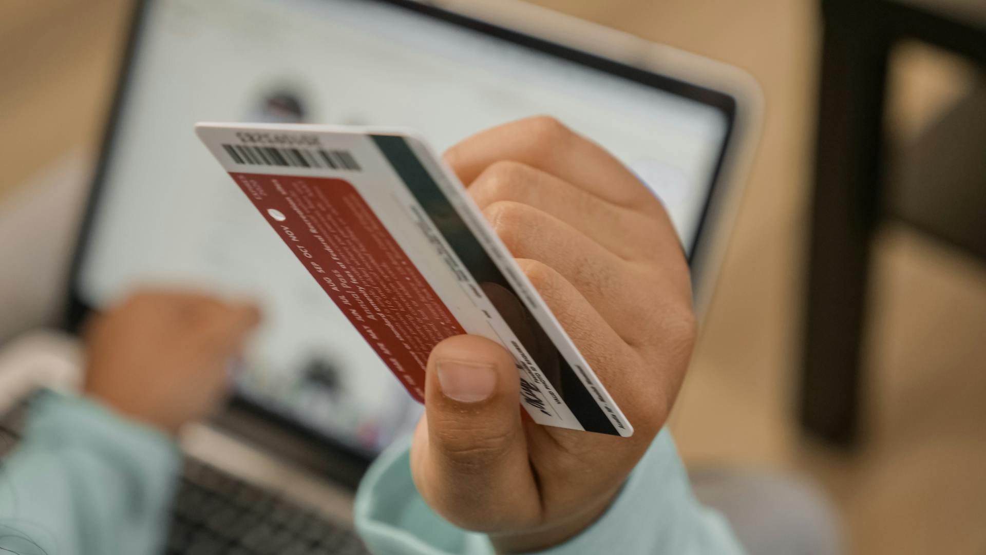 Close-up of hand holding a credit card during an online transaction on a laptop.