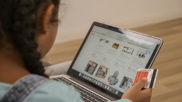 Child using laptop for online shopping, holding a credit card.