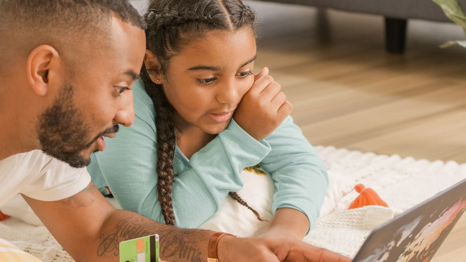 A father and daughter engage in online shopping at home, bonding over technology.