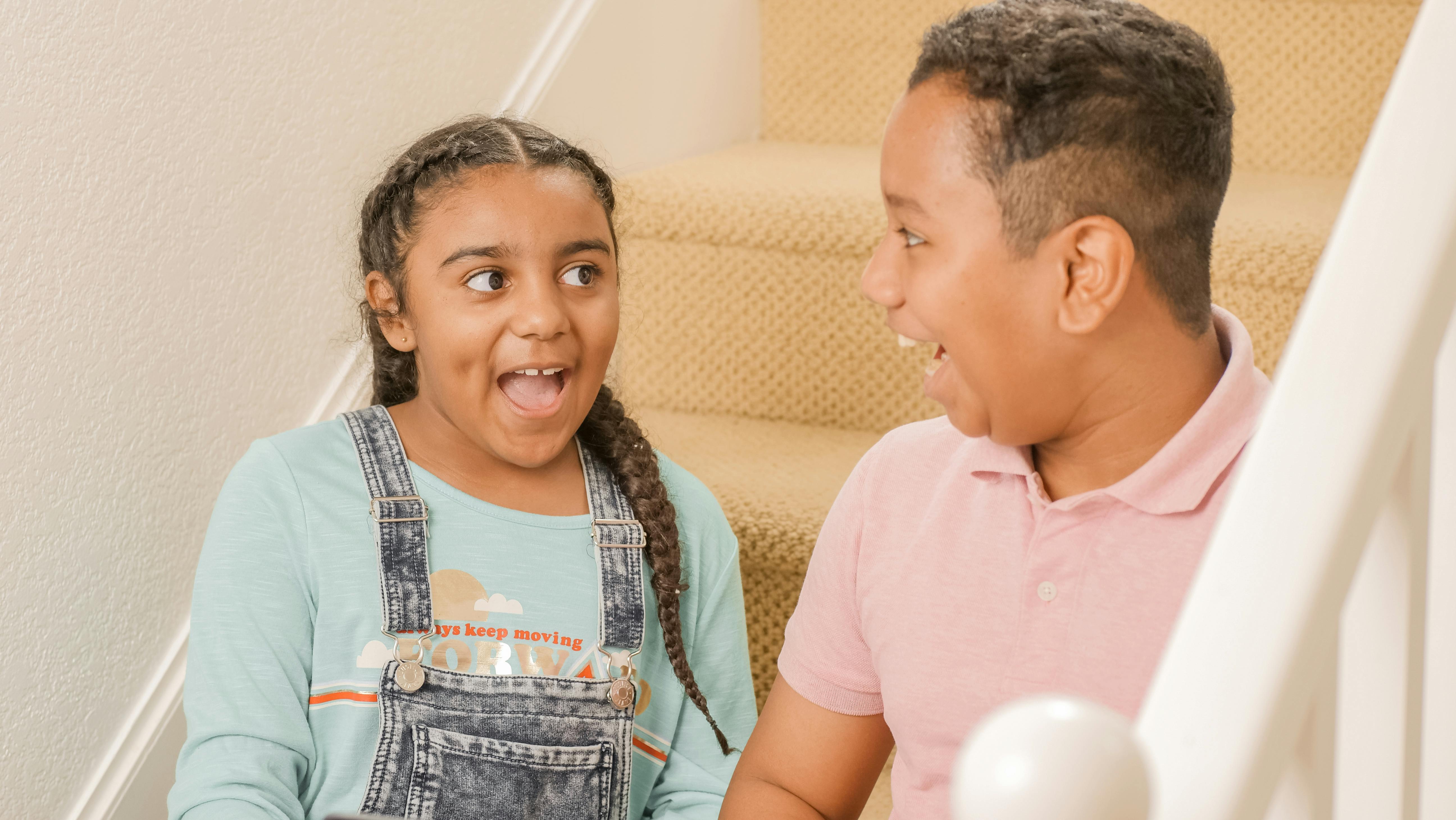 Happy siblings sharing a joyful moment on the staircase indoors.