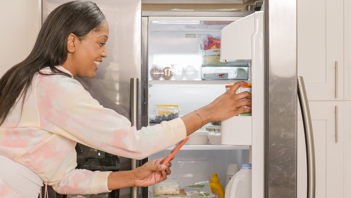 A Woman Holding a Cellphone Beside a Fridge