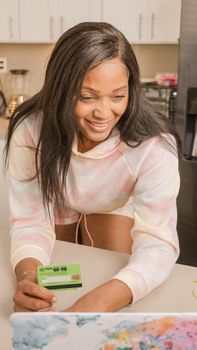 Smiling woman making an online purchase using a credit card in a bright kitchen.