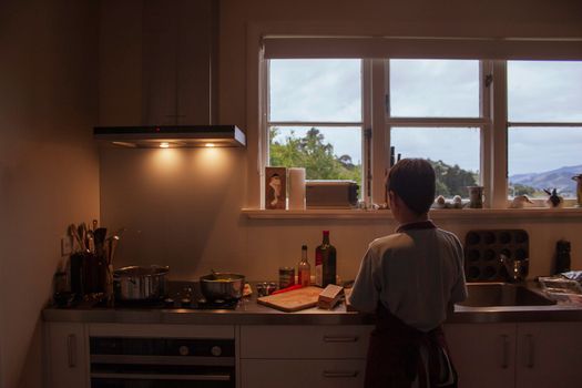 Young boy preparing food in a cozy indoor kitchen setting with scenic outdoor view.