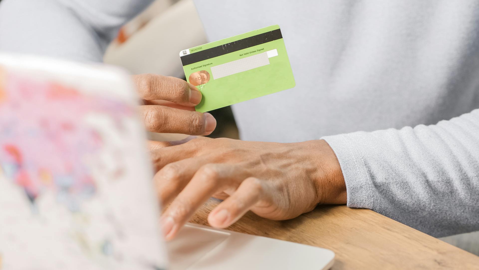 Close-up of hands holding a green credit card for an online purchase using a laptop, depicting secure transactions.