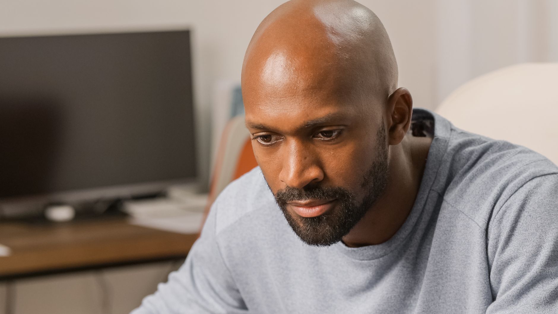 A thoughtful man with a beard and bald head is focused indoors, near a desk with computer.