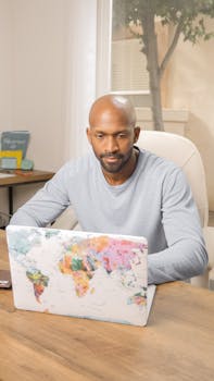 Man in casual attire using a laptop in a bright home office setting for remote work.