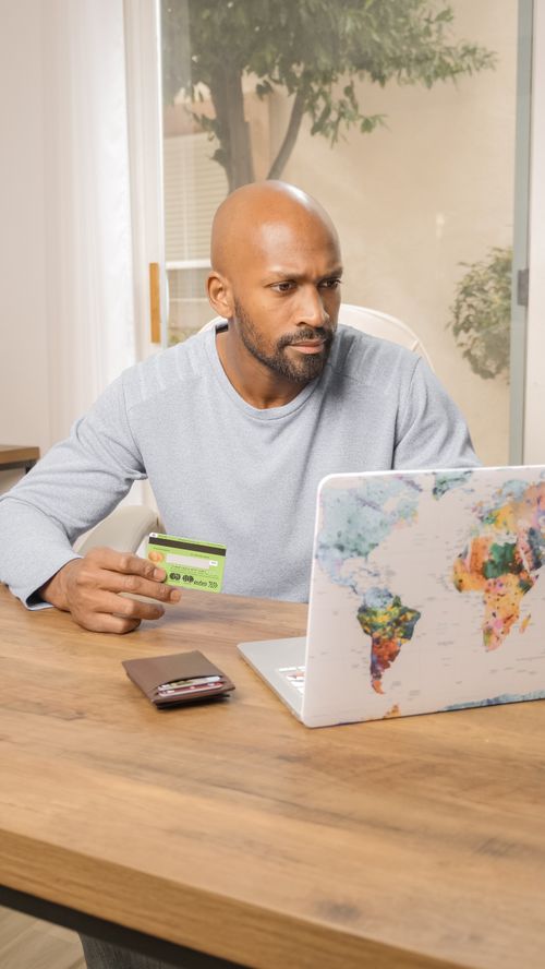 Free Bald man using credit card for online shopping on colorful world map laptop indoors. Stock Photo