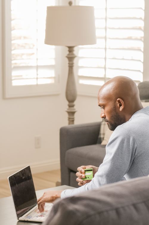 Free An adult man sitting indoors using a laptop and holding a credit card for online shopping. Stock Photo