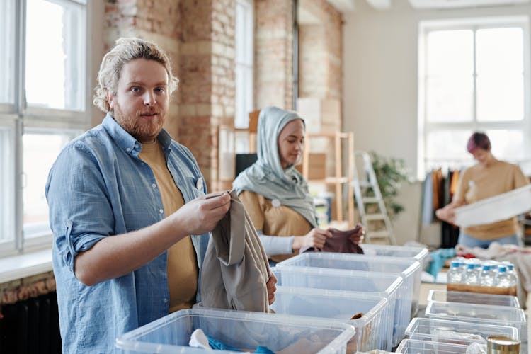 Young Men And Women Sorting Clothes Into Plastic Containers 