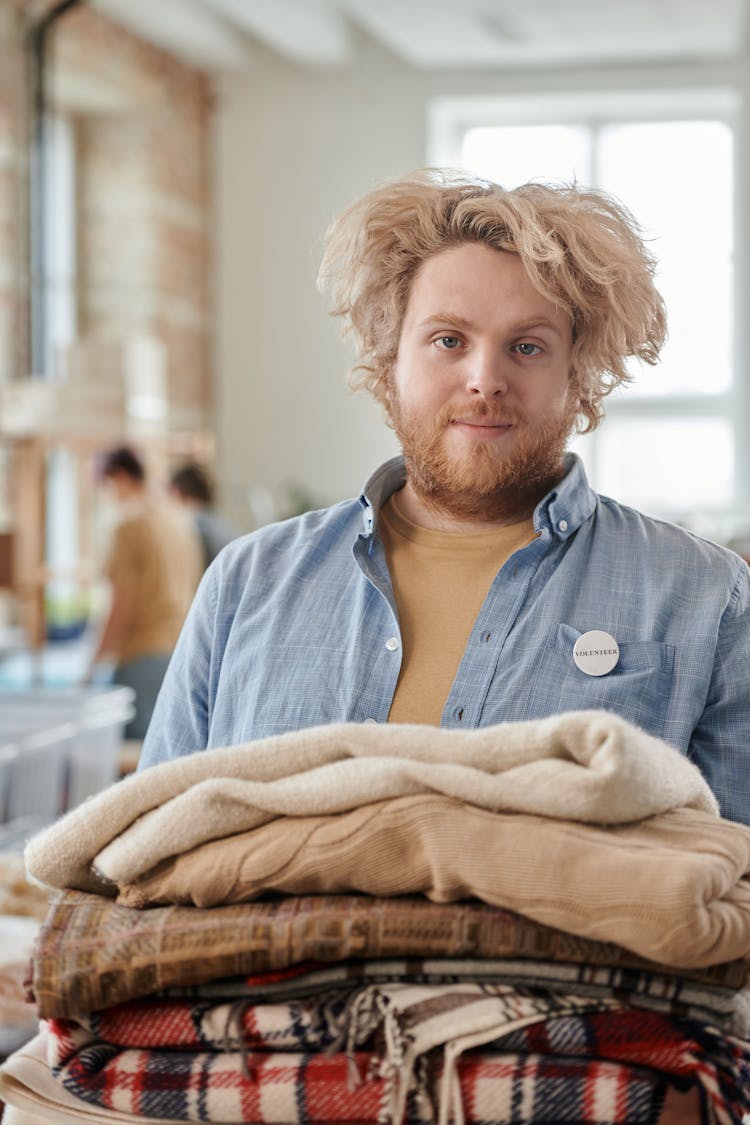 A Bearded Man Holding A Pile Of Folded Scarfs