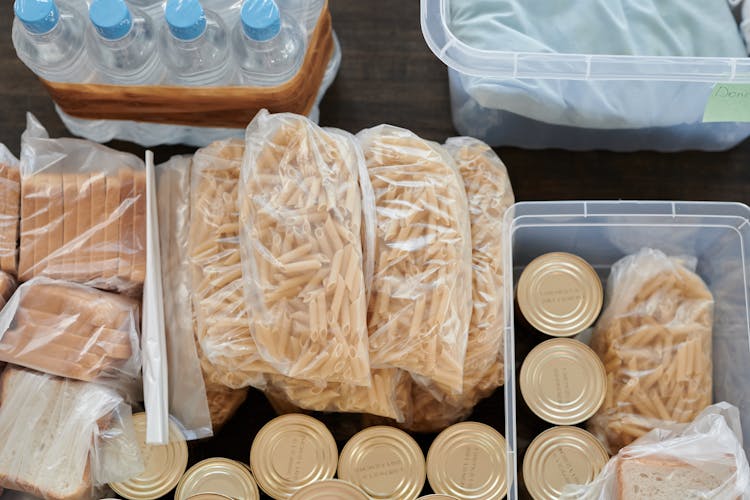 Bags Of Uncooked Macaroni Pasta Beside Canned Foods And Slices Of Bread