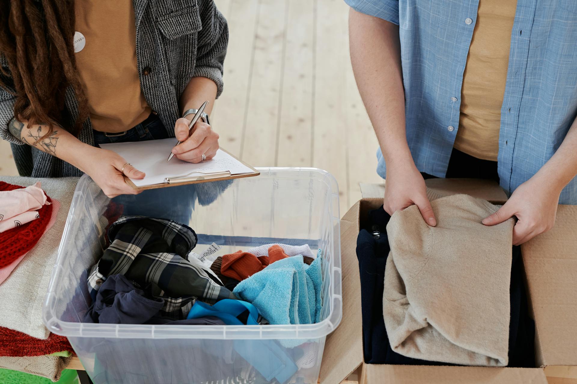 Two volunteers sort and document donated clothes indoors for charity distribution.