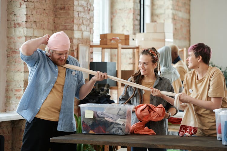 Young Men And Women Having Fun While Volunteering With Sorting Clothing 