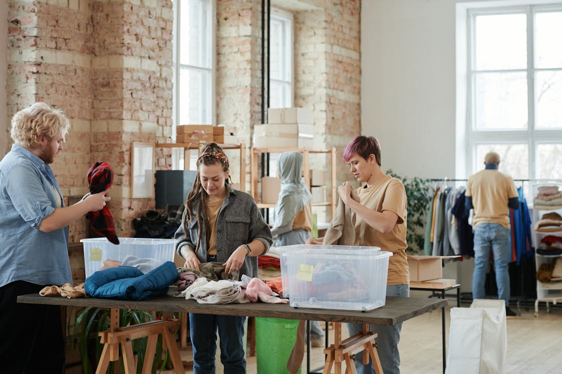 Free Volunteers organizing clothes in a bright, rustic donation center indoors. Stock Photo