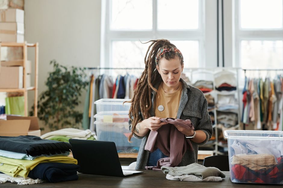 Young woman with dreadlocks sorting clothes in a modern loft. Volunteer work indoors.