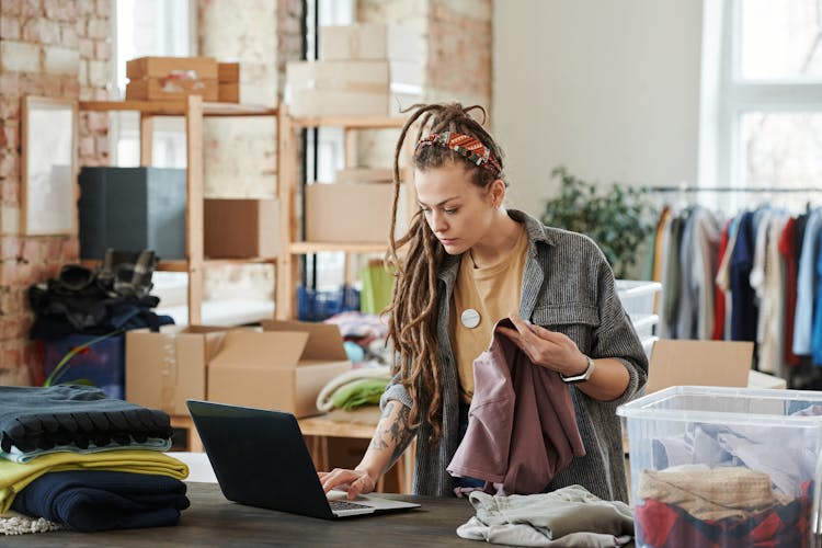 Woman Holding A Shirt While Using A Laptop