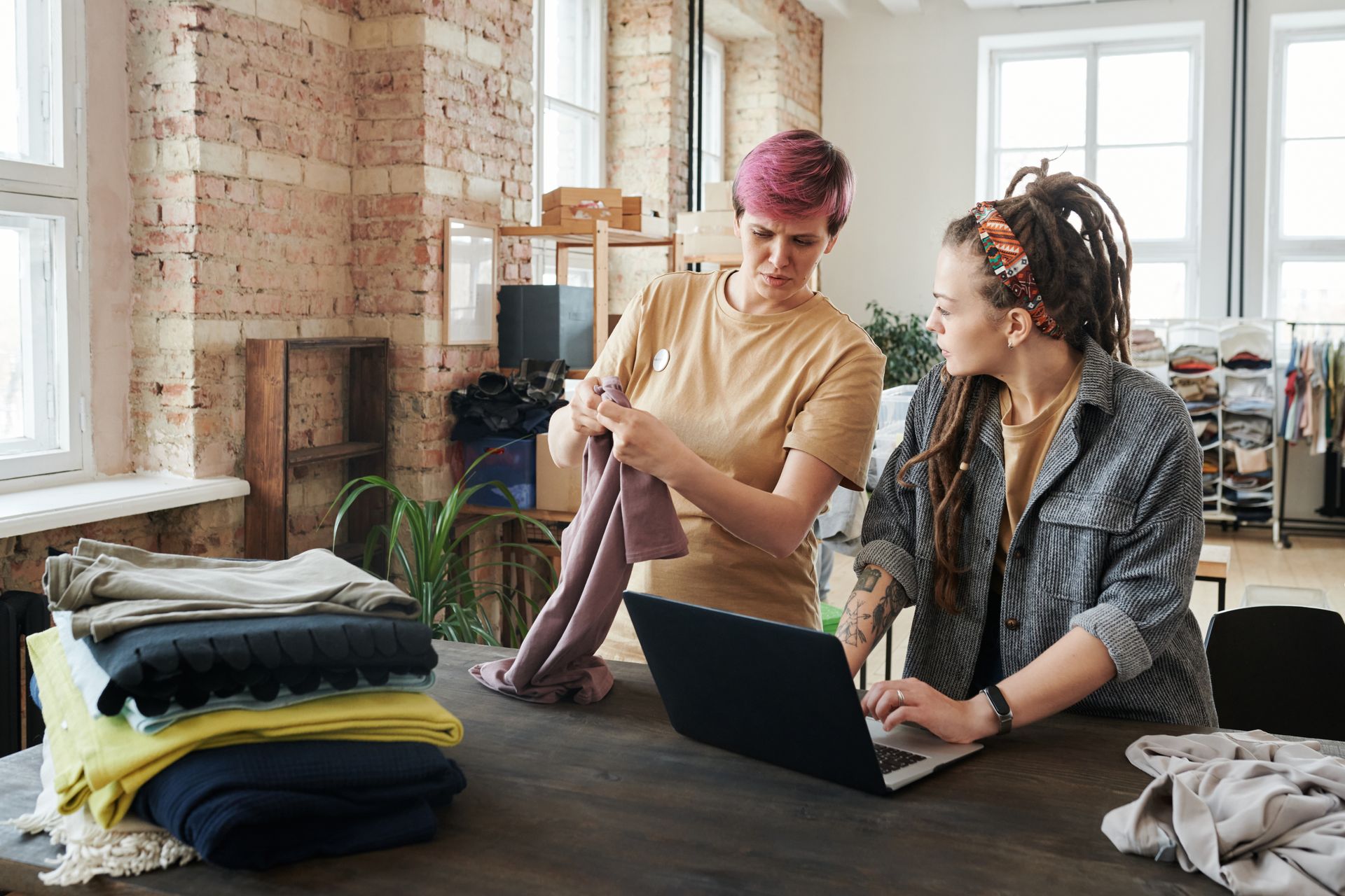 Two women sorting piles of donated clothing in a bright workspace