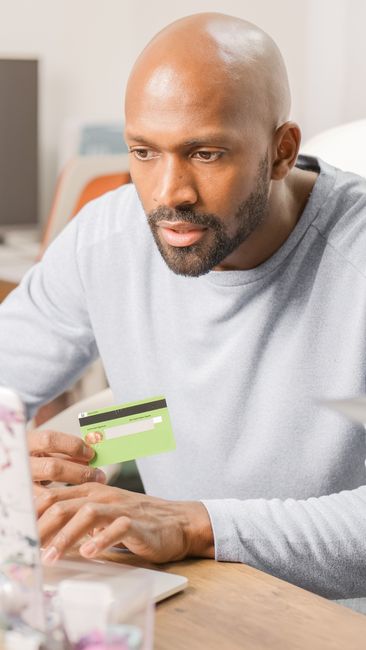 Focused man using credit card for online shopping indoors, showcasing e-commerce convenience. Focused man using credit card for online shopping indoors, showcasing e-commerce convenience.