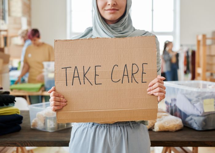 A smiling volunteer holding a 'Take Care' sign at an event