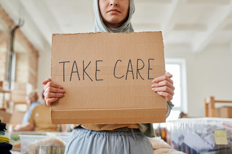 
A Woman In A Hijab Holding A Cardboard Sign