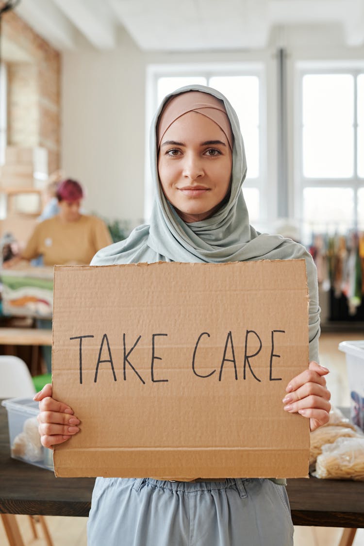 
A Woman In A Hijab Holding A Cardboard Sign