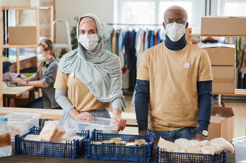 Free Diverse volunteers wearing masks while organizing and packing donation supplies indoors. Stock Photo