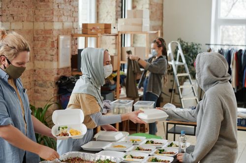 Free Volunteers wearing face masks distribute food in takeaway boxes at a community charity event. Stock Photo