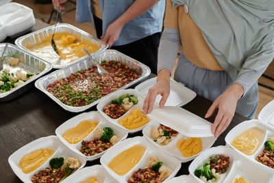 Volunteers, one wearing hijab, portioning prepared meals into takeaway boxes