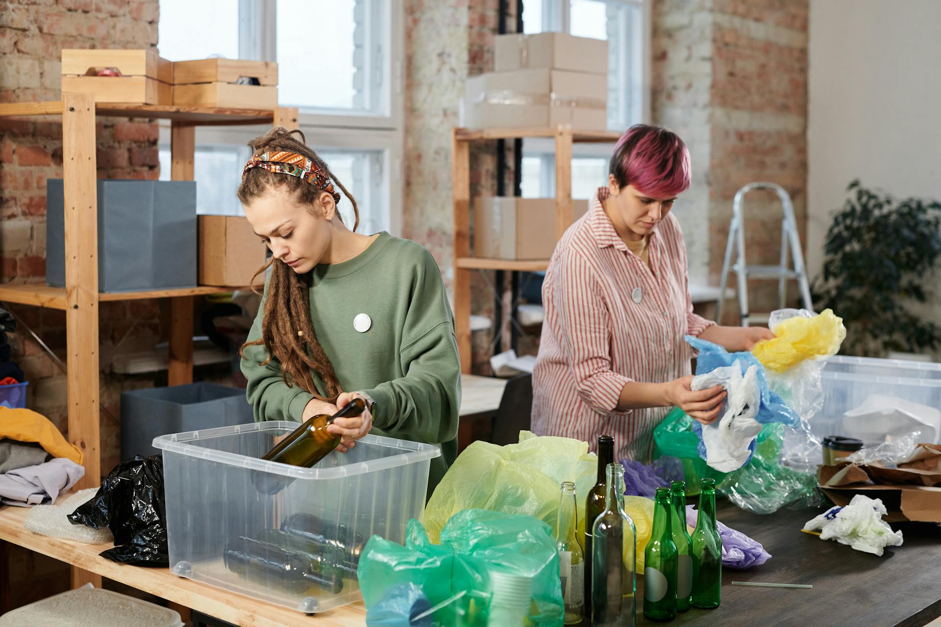 Two women sorting glass and plastic waste in an indoor recycling center.