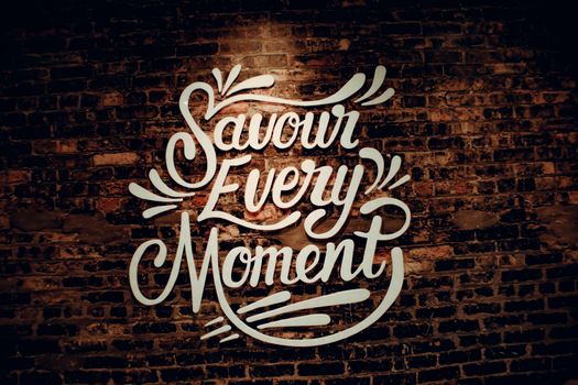 White creative signboard with Savour Every Moment inscription with decorative elements hanging on shabby brown brick wall of contemporary cafeteria