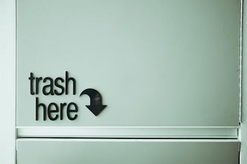 Black inscription with pointer indicating spot for trash disposal on white door of rubbish bin located in light public place