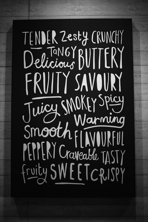 Black and white of creative signboard with various written words describing taste sensations placed at wall in modern light cafeteria