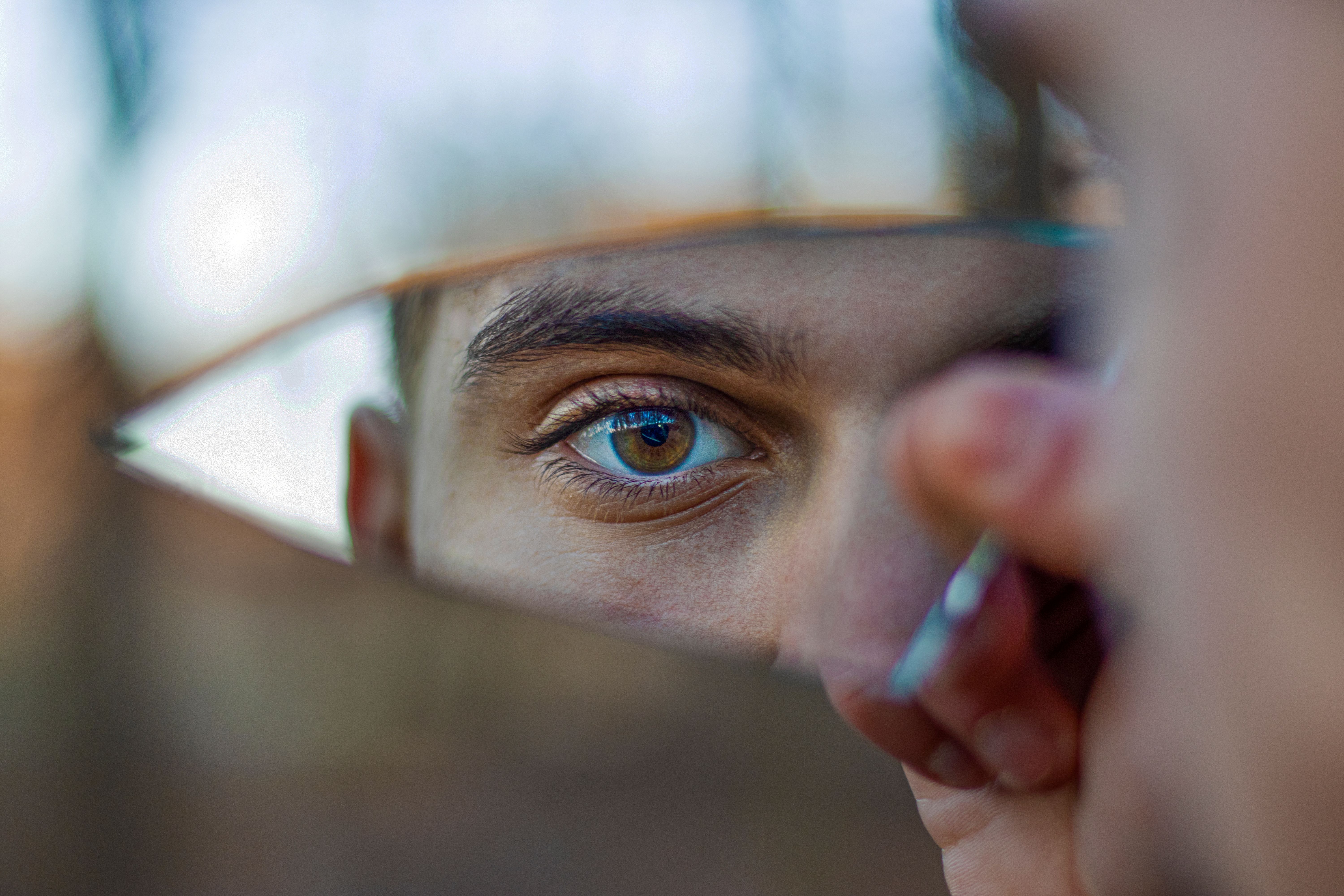 A striking portrait reflecting a blue eye in a piece of broken mirror outdoors.