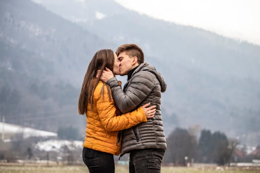Romantic couple kissing outdoors against a backdrop of scenic mountains in winter.