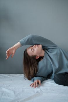 Young female in casual outfit lying on comfortable bed with closed eyes against gray background