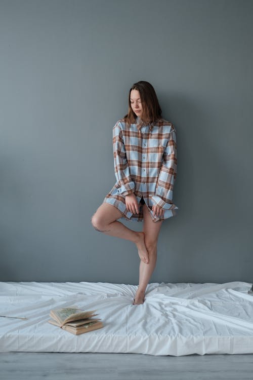 Woman in Blue and Brown Plaid Long Sleeve Shirt Standing on White Mattress