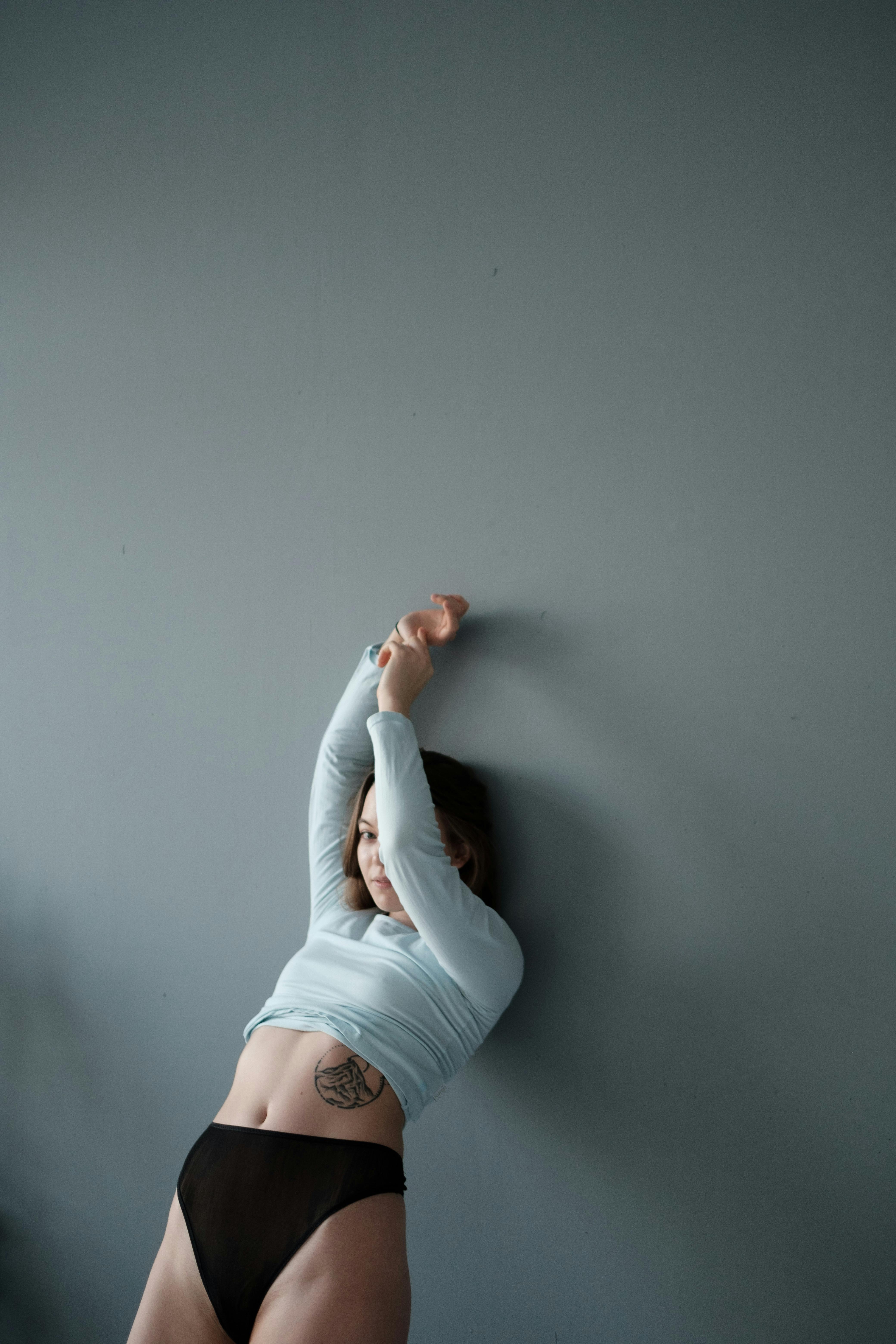 a woman in white long sleeve shirt and black panty leaning on wall