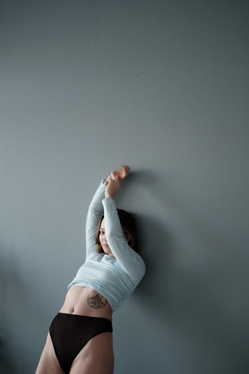 A Woman in White Long Sleeve Shirt and Black Panty Leaning on Wall