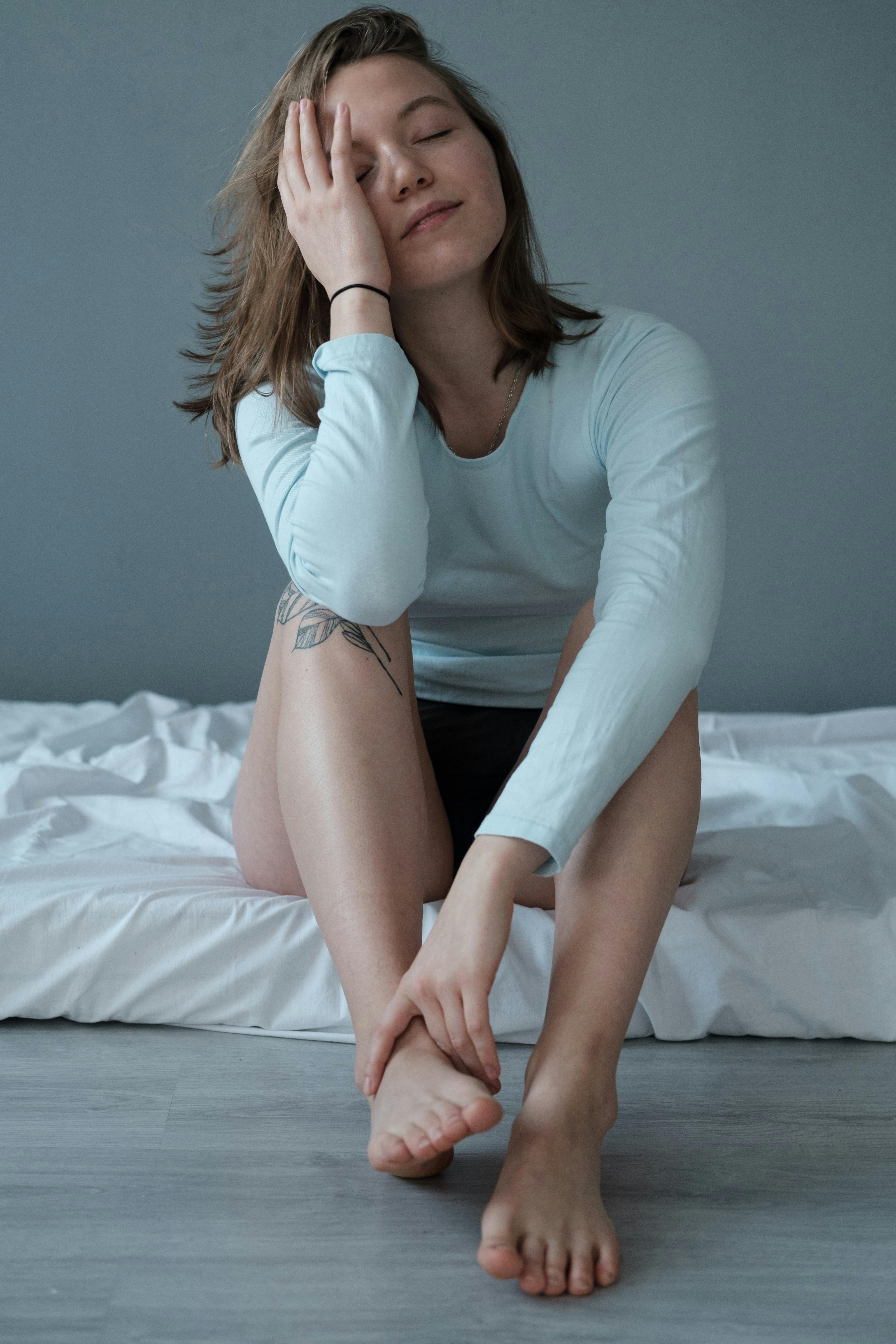 Calm woman with closed eyes sitting indoors, hand on face, tattoo visible.