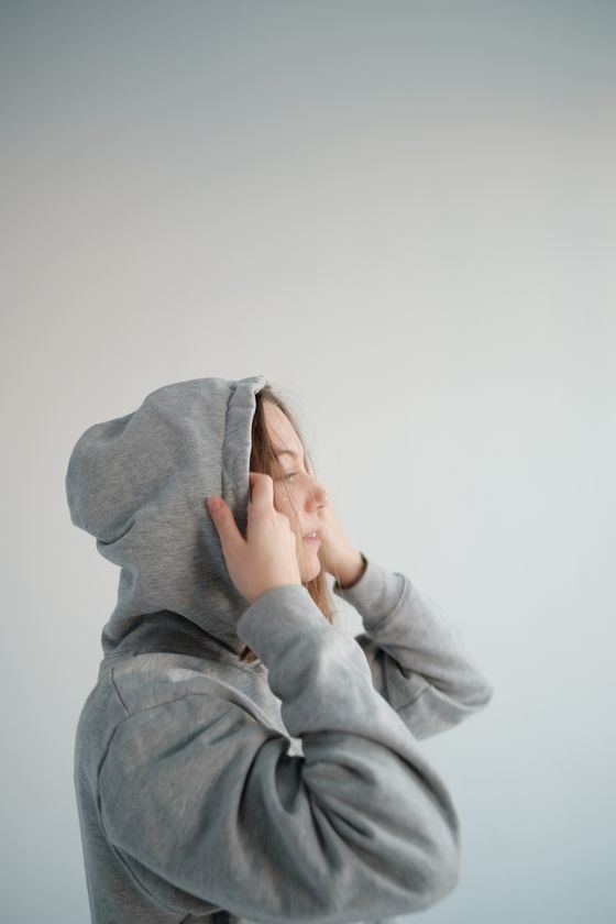 Person pulling up the hood of a grey sweatshirt in a light studio, photo by Alena Shekhovtcova on Pexels