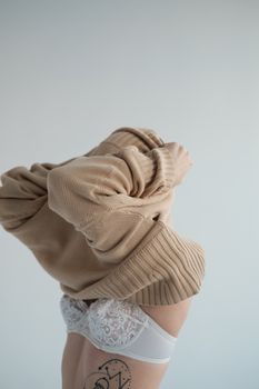 Side view of unrecognizable female with tattoo in lingerie putting on warm sweater against white background